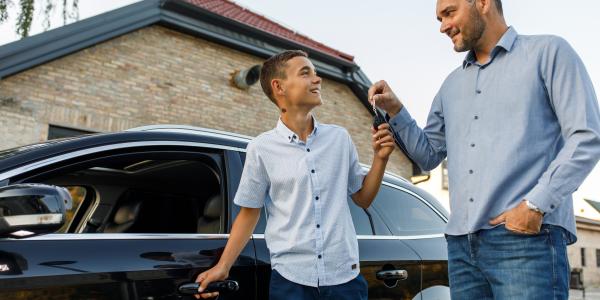 Caring adult man handing car keys to his teenage son while they are standing by the car, about to let him drive for the first time.