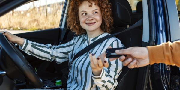 Young person receiving car keys from a person while sitting in new car.