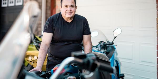 Mature person working on their vintage motorcycle in front of his garage. 