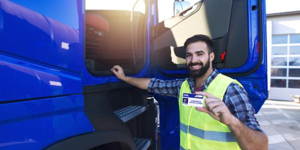 Truck driver candidate standing in front of truck, showing CDL driving license. 