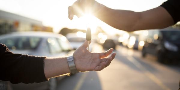 A person hands car keys to another person after a vehicle sale.