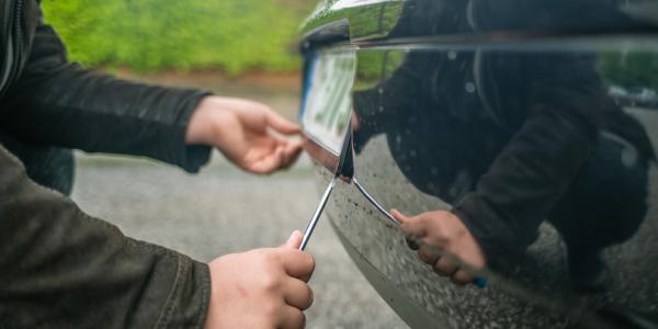 A person stealing the license plate off of a car with a screwdriver.