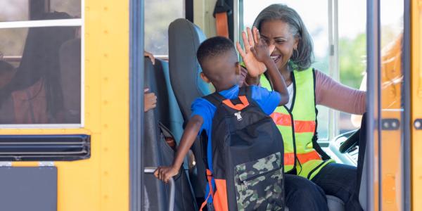 Bus driver high fives new student stepping on bus.